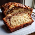 Close-up of a slice of moist apple bread with a visible cinnamon swirl and golden-brown crust.
