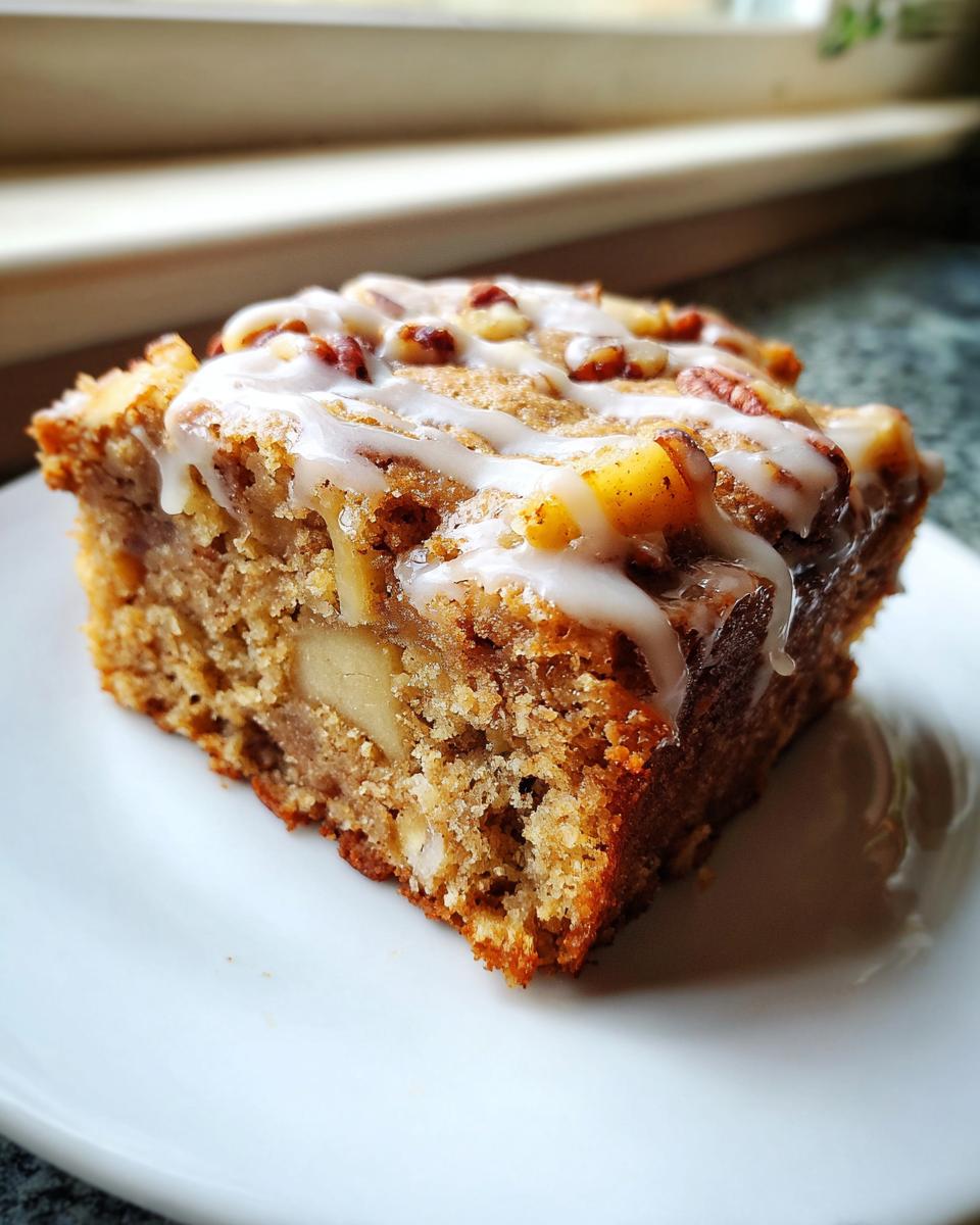 Close-up of a single serving of moist apple brownies topped with white glaze and pecans.