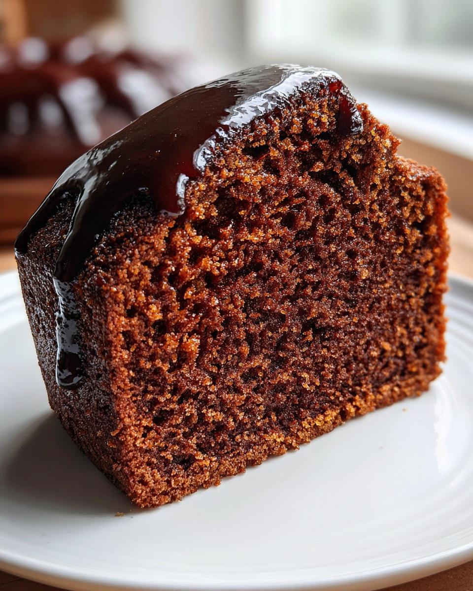 Close-up of a moist slice of gingerbread cake topped with rich, dark chocolate glaze.