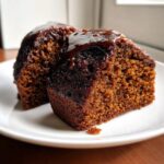 Two moist slices of dark gingerbread cake topped with a rich, glossy glaze, served on a white plate.