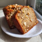 Two slices of moist hawaiian banana bread topped with nuts, served on a small white plate.