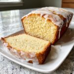 A slice cut from a loaf of moist lemon pound cake topped with thick white glaze.