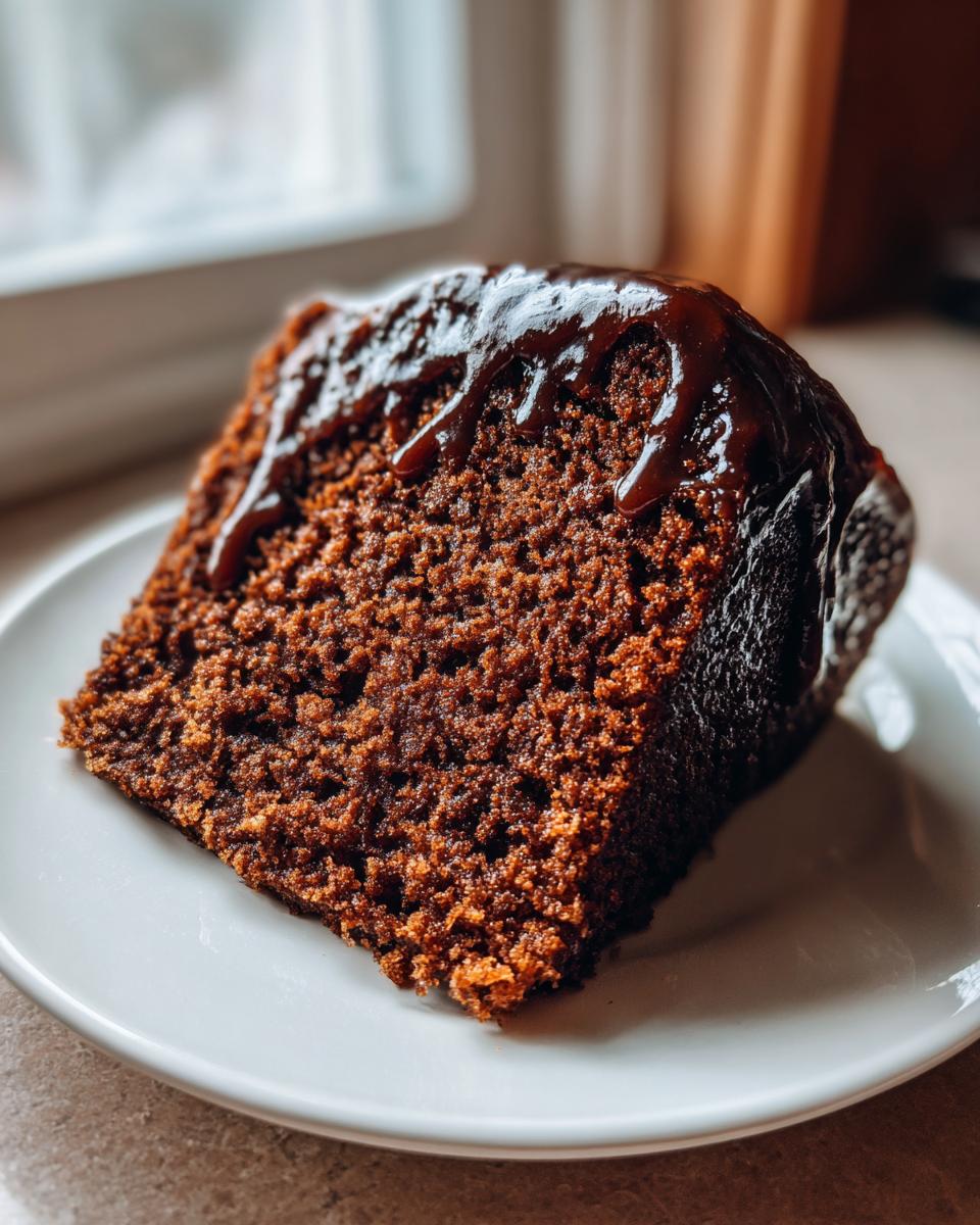 Close-up of a moist slice of dark gingerbread cake topped with a rich, dripping chocolate or molasses glaze.