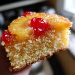 Close-up of a moist slice of pineapple upside down cake topped with caramelized pineapple and bright red maraschino cherries.