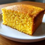 Close-up of a golden, moist slice of sourdough cornbread on a white plate.