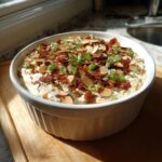 A creamy Neiman Marcus dip served in a white ruffled bowl, topped generously with bacon bits, sliced almonds, and green onions.
