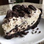A decadent slice of no-bake oreo cheesecake with a thick Oreo crust and creamy filling, topped with crumbs and cookies.