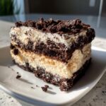 A close-up slice of layered Oreo dirt cake showing dark chocolate cookie crumbs and creamy vanilla filling.