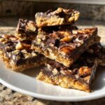 A stack of rich pecan pie bark squares topped with chocolate drizzle and whole pecans.