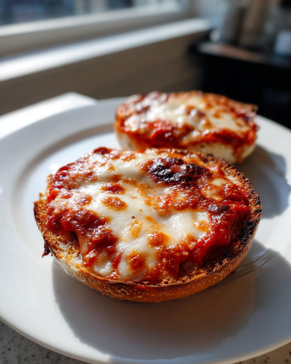Two halves of toasted bagel topped with tomato sauce and bubbly, melted mozzarella cheese, ready to eat as pizza bagels.