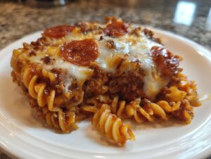 A close-up serving of pizza pasta bake featuring rotini pasta, meat sauce, melted mozzarella, and pepperoni slices.