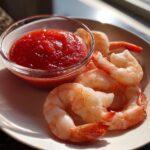 Plump, cooked shrimp arranged next to a small glass bowl of bright red shrimp cocktail sauce.
