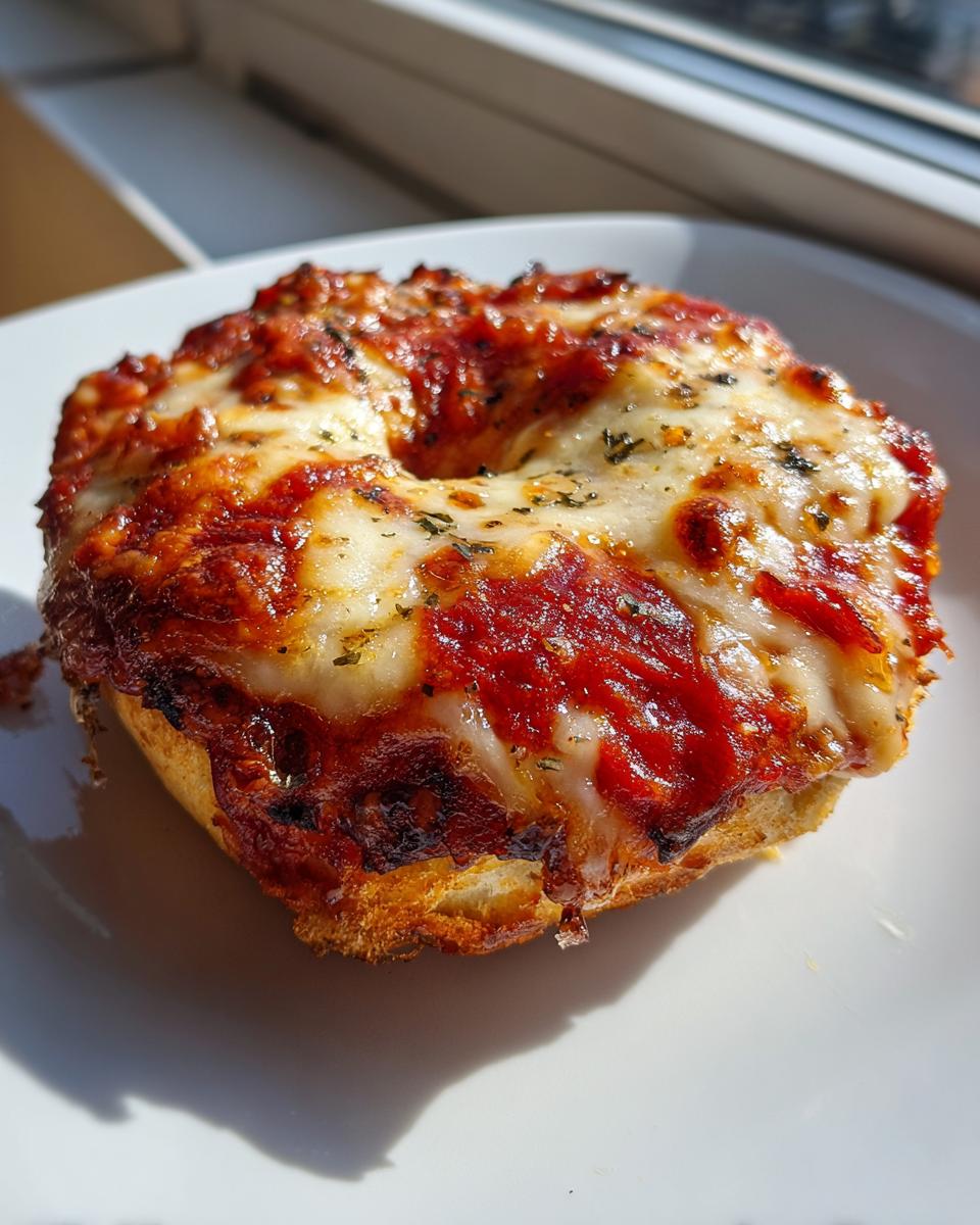 Close-up of a perfectly melted pizza bagels half topped with bubbling cheese, rich tomato sauce, and herbs.