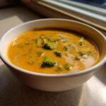 Close-up of a bowl of rich, orange-colored broccoli cheddar soup with visible florets.