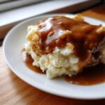 A close-up of creamy mashed potatoes topped with a piece of meat and smothered in rich, brown chicken gravy.