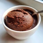 A scoop of thick, rich homemade chocolate pudding served in a small white bowl with a spoon.