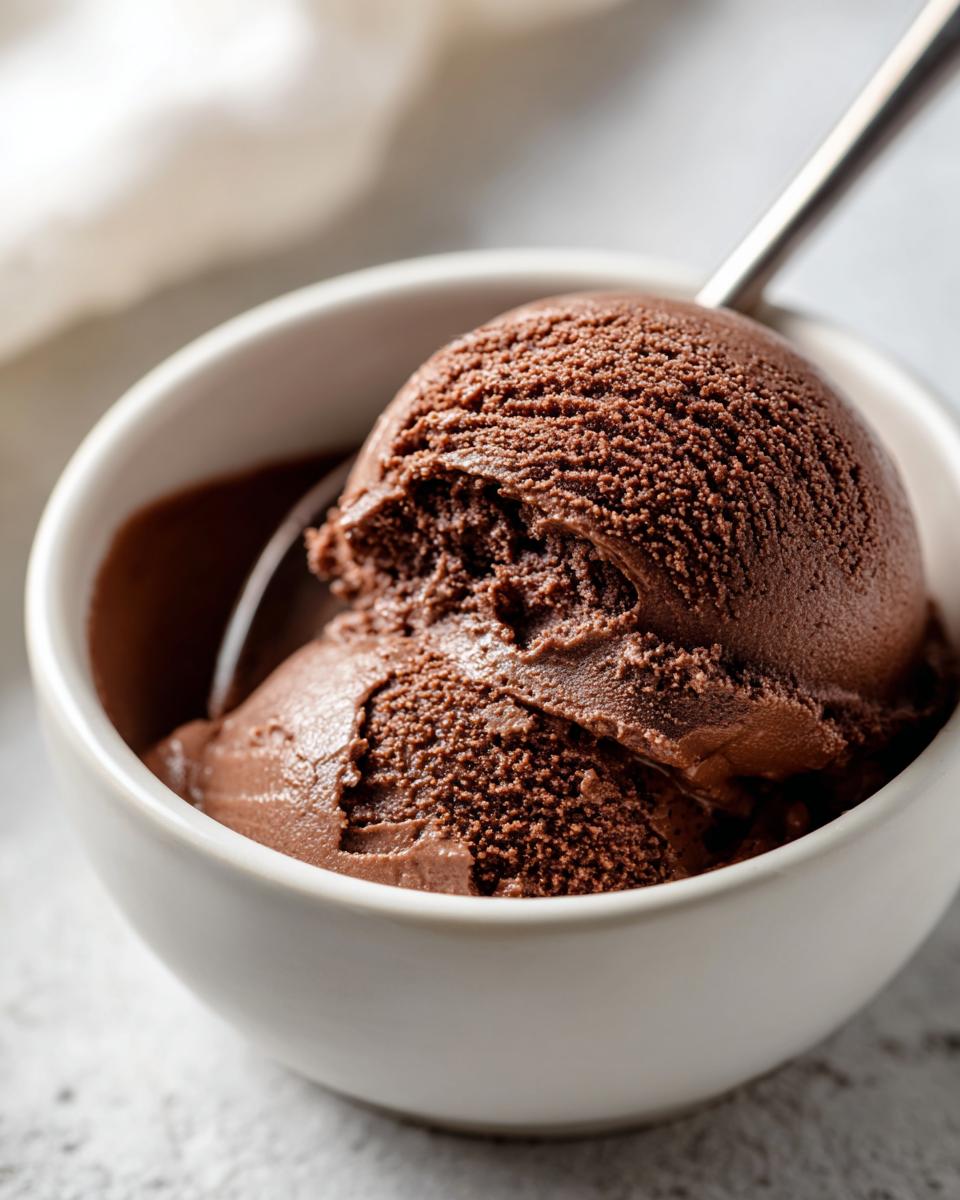 Two scoops of rich, dark homemade chocolate pudding served in a white bowl with a spoon.