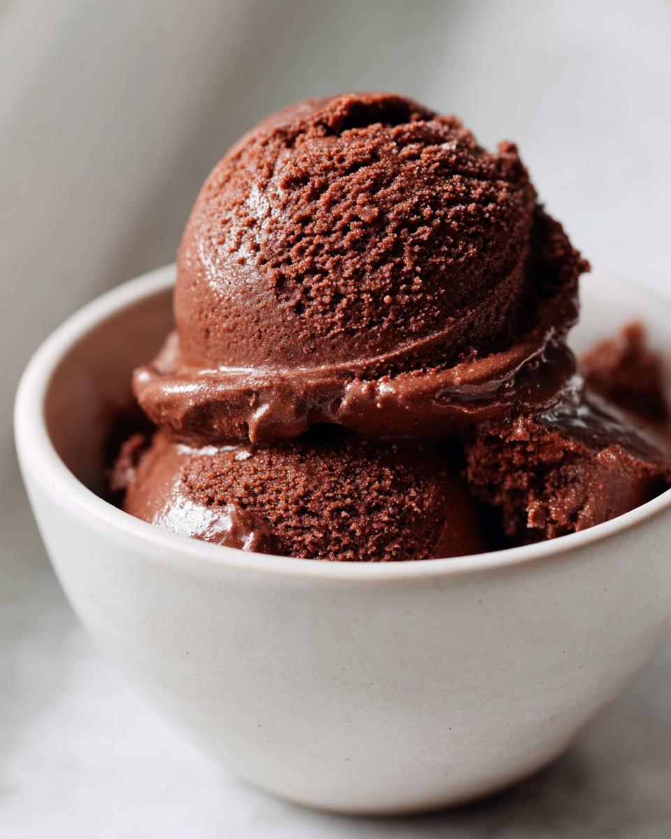 Three scoops of rich, dark homemade chocolate pudding served in a small, light-colored bowl.