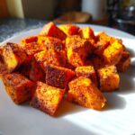 Close-up of bright orange, seasoned roasted sweet potato cubes piled on a white plate.