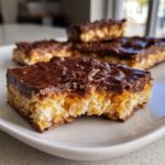 A close-up of a piece of saltine cracker toffee with a bite taken out, showing the layers of cracker, caramel, and chocolate.