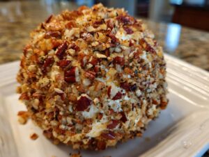 A close-up of a perfectly formed cheese ball recipe coated entirely in chopped pecans and herbs.
