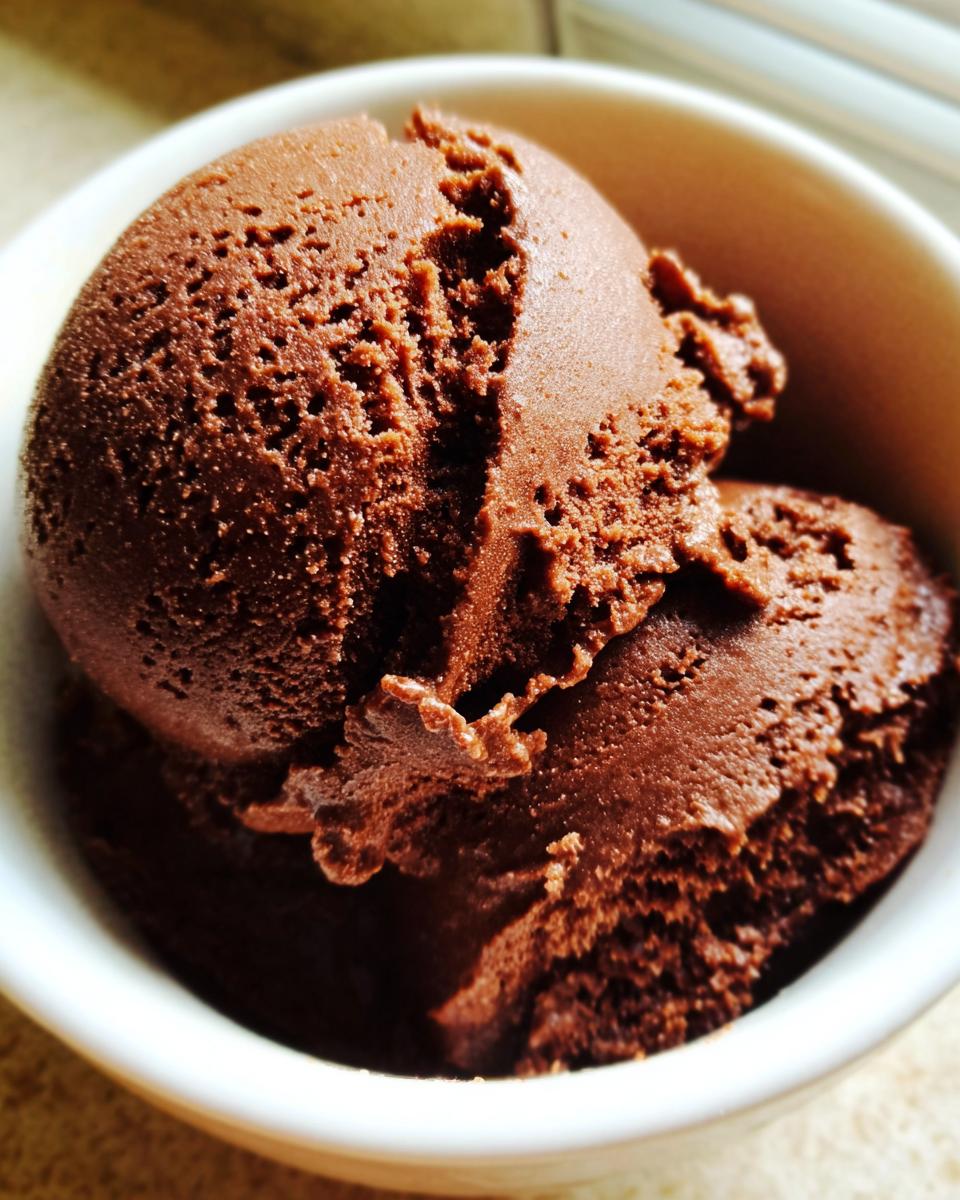 Close-up of two scoops of rich, dark homemade chocolate pudding served in a white bowl.