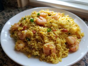A close-up of a generous serving of yellow shrimp fried rice recipe, topped with pink shrimp and green onions.