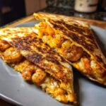 Two halves of a perfectly grilled shrimp quesadilla overflowing with seasoned shrimp and melted cheese.