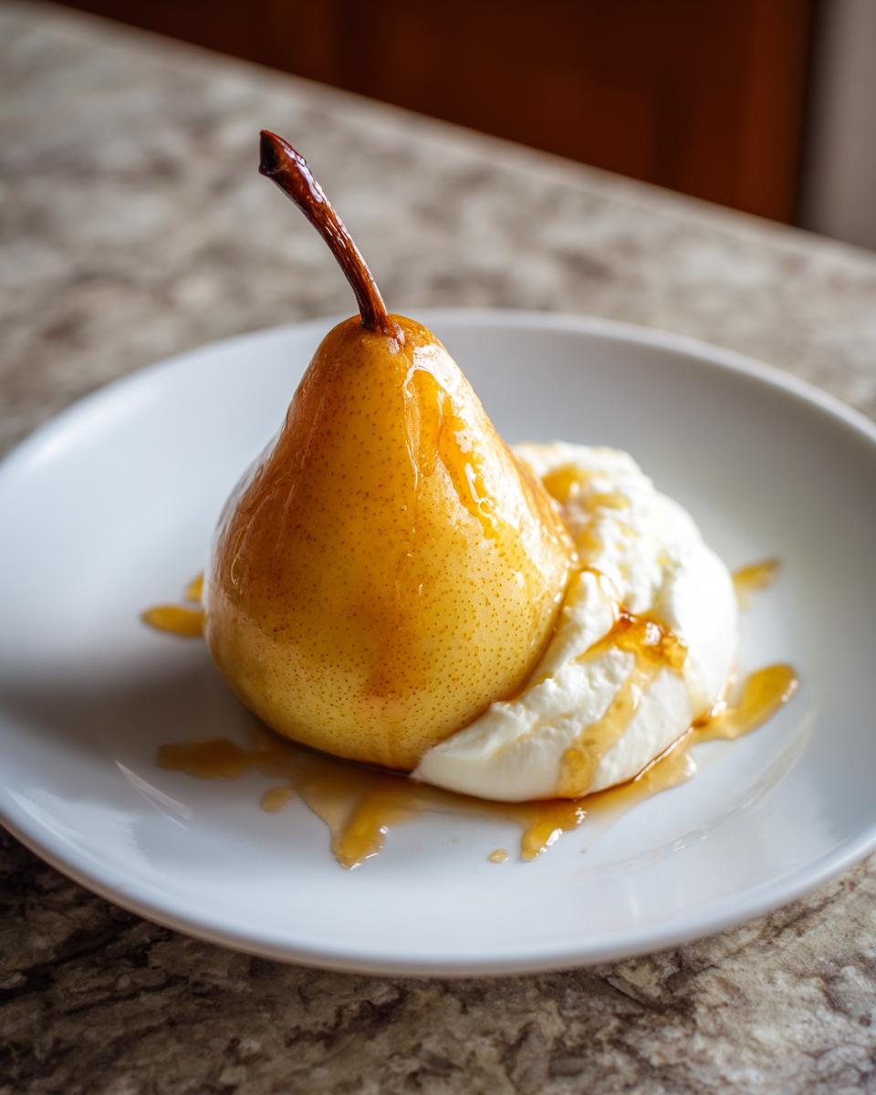 A single, beautifully glazed poached pear served on a white plate alongside a dollop of whipped cream.