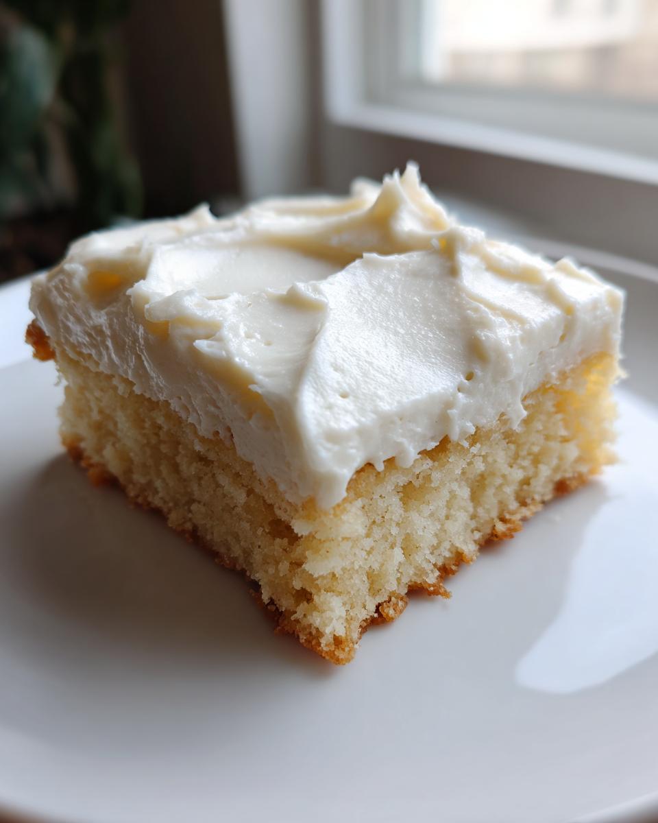 A close-up of one square piece of light, fluffy sugar cookie bars topped with thick white frosting.