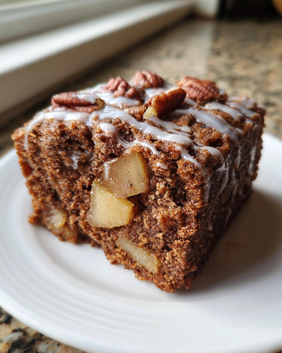 A single square of rich, dark apple brownies topped with white glaze and pecans.
