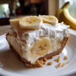 A close-up of a slice of banana cream pie recipe topped with whipped cream and fresh banana slices.