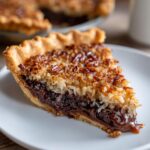 A close-up of a slice of german chocolate pie showing a gooey chocolate layer and a thick coconut pecan topping.