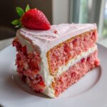 A perfect slice of pink strawberry cake layered with white frosting and topped with a fresh strawberry.