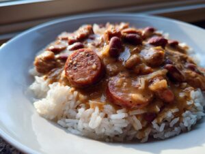 Close-up of a white bowl filled with fluffy white rice topped with creamy slow cooker red beans and rice and slices of andouille sausage.