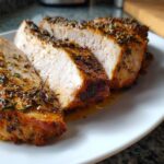 Three thick slices of juicy slow cooker turkey breast, seasoned with herbs, resting on a white plate.