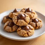 A stack of soft peanut butter blossoms rolled in sugar, each topped with a melted chocolate kiss.