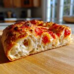 Close-up of a thick slice of pizza made with sourdough discard pizza dough, showing a highly airy, open crumb structure.