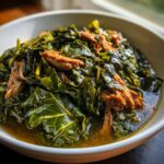 Close-up of tender, dark green collard greens stewed in broth with pieces of shredded smoked meat.