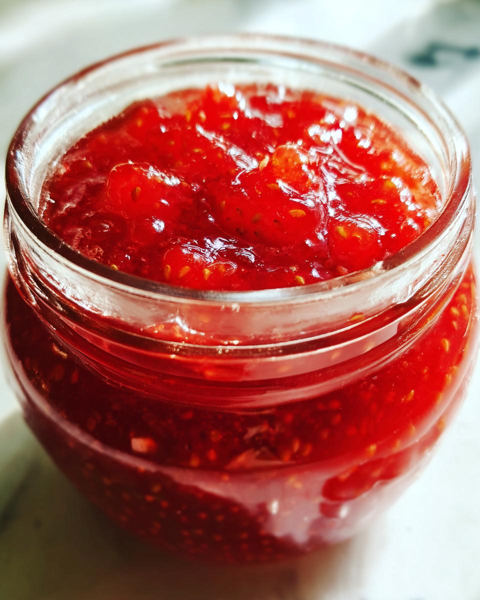 A close-up view of vibrant, chunky strawberry freezer jam filling a small glass jar.