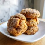 A stack of four soft, crinkly persimmon cookies coated in cinnamon sugar resting on a white square plate.