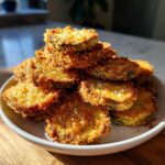A tempting pile of super crispy fried pickles, golden brown and seasoned, stacked high on a white plate.