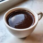 Close-up of a thick, dark, glossy french hot chocolate served in a white ceramic mug.