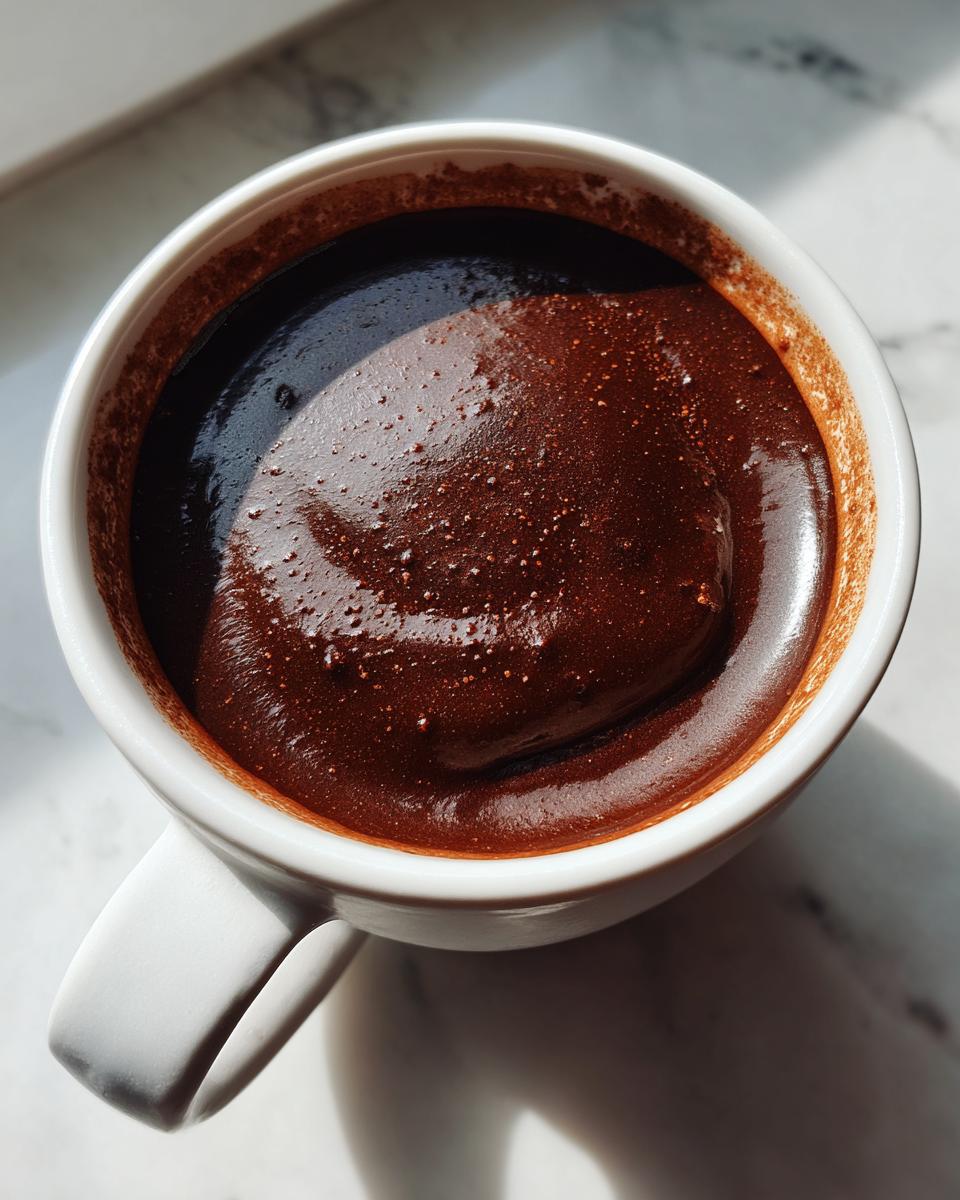 Overhead close-up of thick, dark, rich french hot chocolate with a foamy top in a white mug.