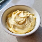A close-up of thick, pale yellow homemade mayonnaise swirled beautifully in a small white bowl.