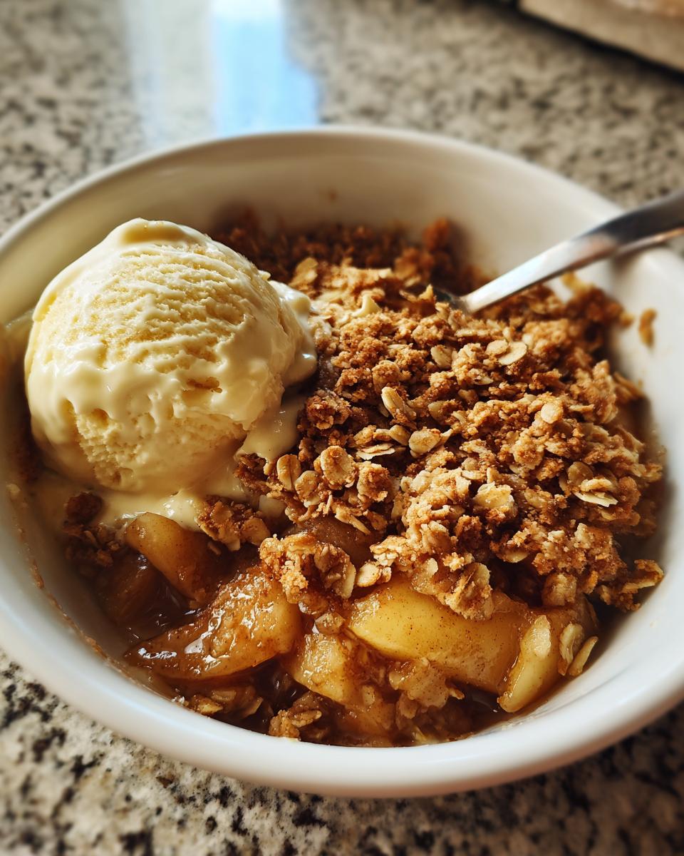 Close-up of warm apple crisp topped with a melting scoop of vanilla ice cream in a white bowl.