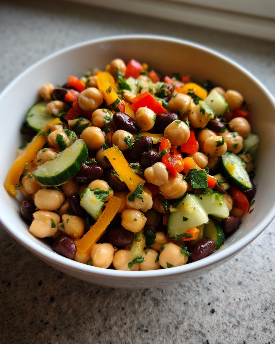 Close-up of a fresh bean salad featuring chickpeas, kidney beans, cucumber, and bell peppers in a white bowl.