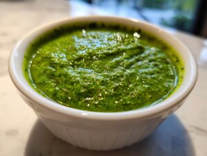 Close-up of a bright green, textured cilantro lime sauce served in a small white bowl.