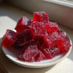 Close-up of sparkling, deep red, sugar-coated cubes of cinnamon rock candy piled on a small white plate.