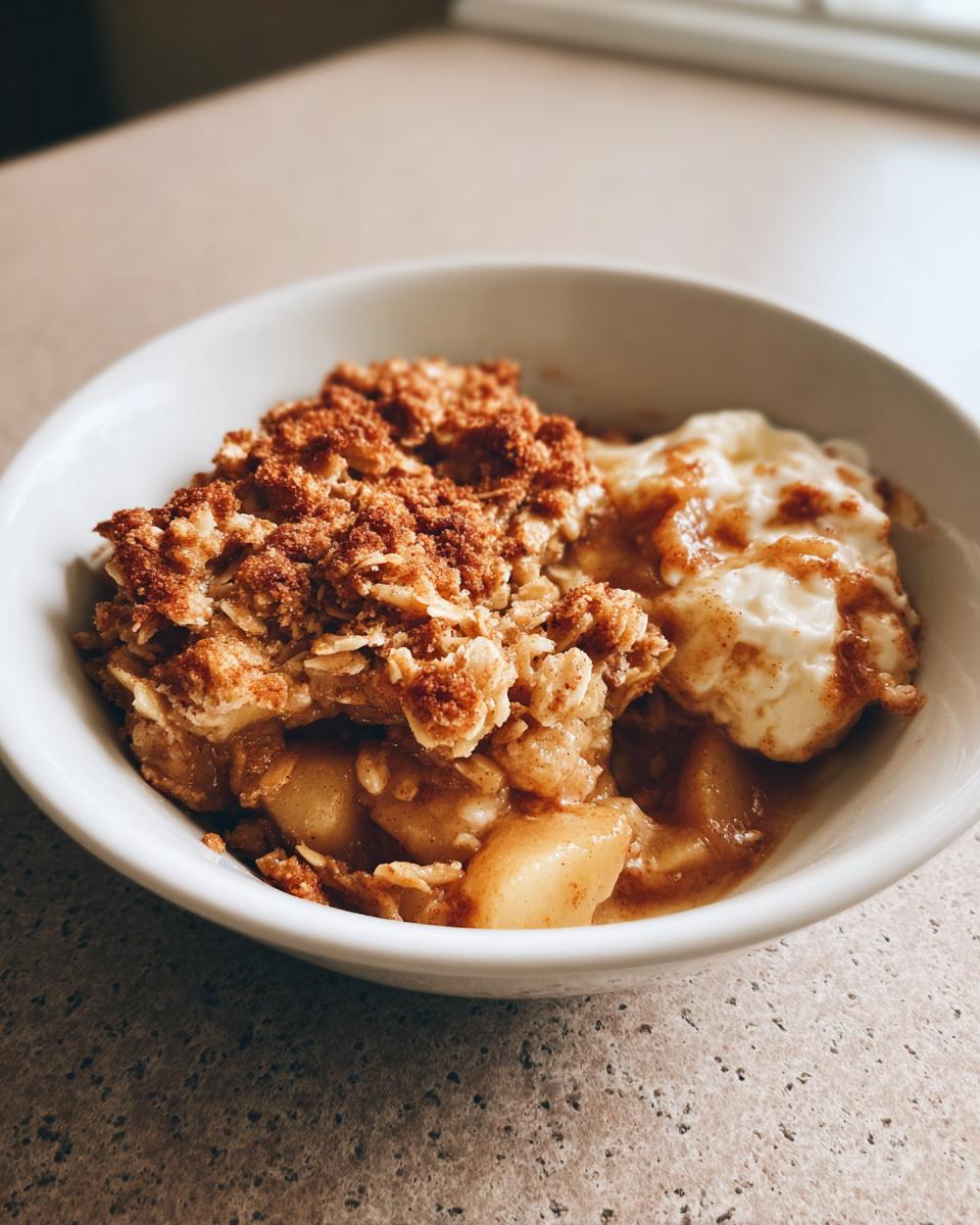 Close-up of a warm serving of apple crisp with a crunchy oat topping and a scoop of melting vanilla ice cream.